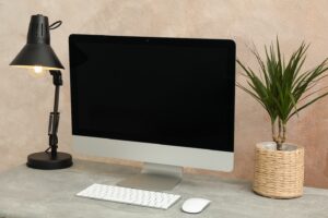 Computer, plant and lamp on wooden table. Workplace room